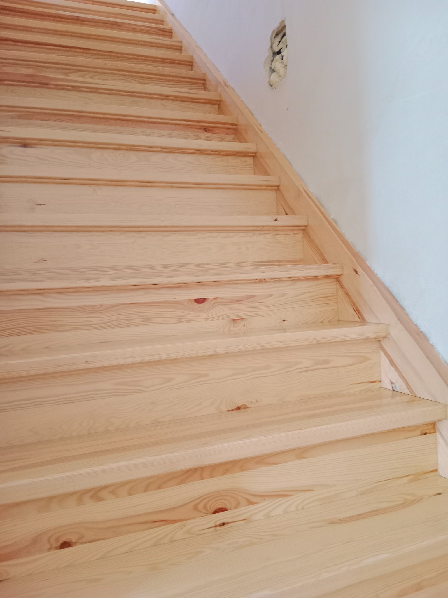 Jasne, drewniane schody z widocznym uszkodzeniem ściany w tle