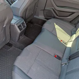 Wnętrze samochodu Peugeot 508, widok na tylną kanapę z szarej tapicerki materiałowej z elementami skóry, czarne dywaniki z wzorem plastra miodu i kratki wentylacyjne w podłokietniku.