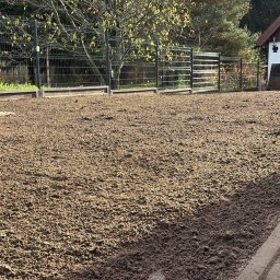 CZYSTY OGRÓD KAROL WIERZBICKI - Przygotowany teren pod trawnik z widoczną ziemią, ogrodzeniem i budynkiem gospodarczym w tle. Świeżo przekopana gleba czeka na zasiew trawy.