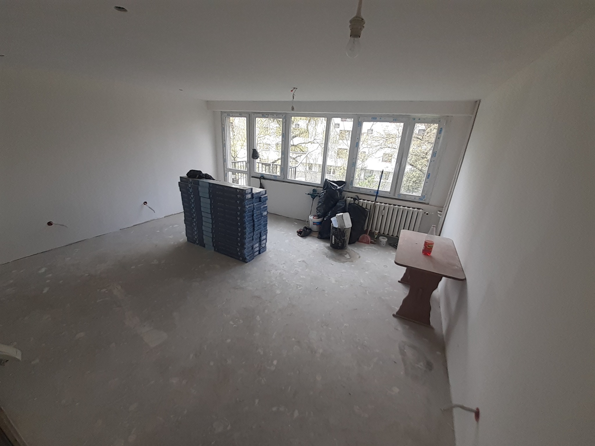 Pokój w trakcie remontu: ściany przygotowane pod wykończenie, na podłodze widoczne ślady prac, ułożone płyty gipsowo-kartonowe, widoczne także narzędzia i materiały budowlane oraz prowizoryczny...