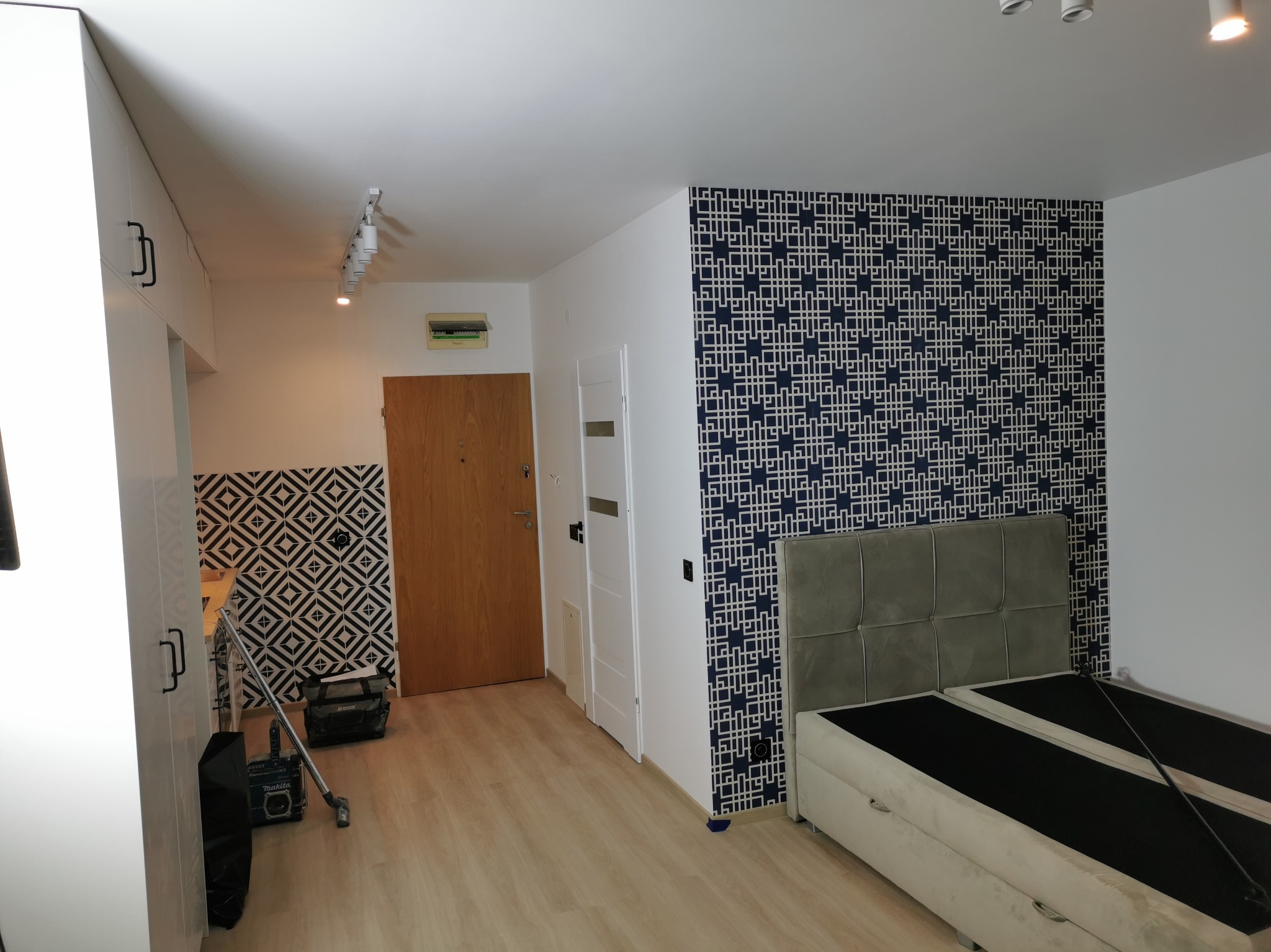 Nowoczesne wnętrze po remoncie: wzorzysta tapeta w geometryczne motywy, jasne panele podłogowe, białe meble i narzędzia po pracy. Widok na odnowione pomieszczenie.