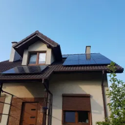 Dom jednorodzinny z brązowym dachem pokrytym panelami fotowoltaicznymi, widok z dołu w słoneczny dzień.