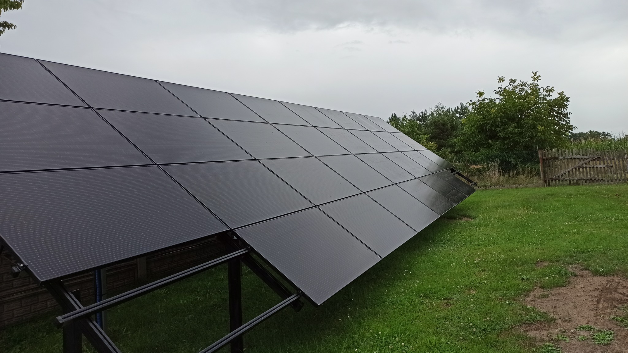 Czarny panel fotowoltaiczny na metalowej konstrukcji zamontowany na trawniku we Wrocławiu, widok z dołu w pochmurny dzień.