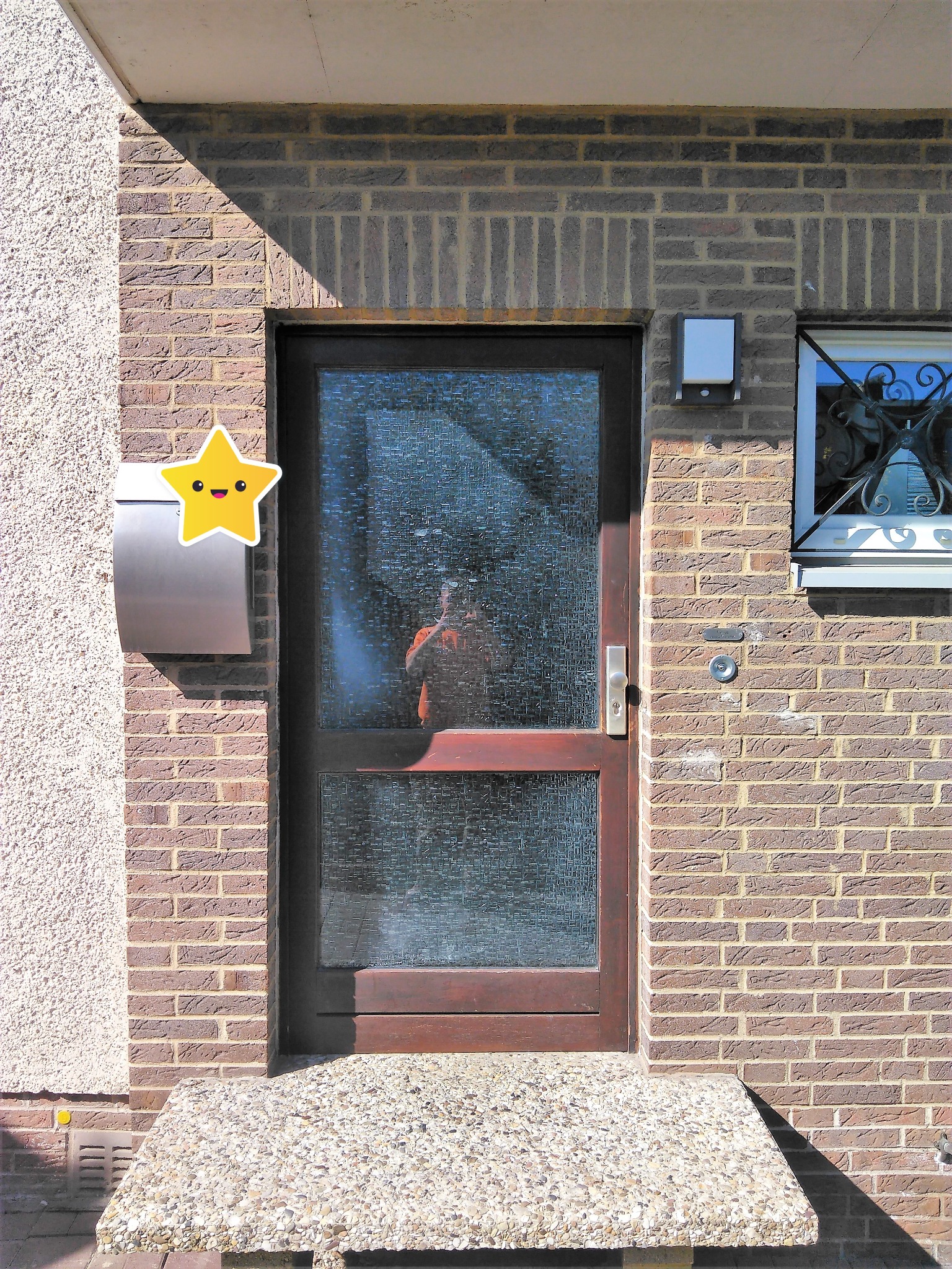 Wejście do domu w Gliwicach z brązowymi drzwiami szklanymi o wzorzystej fakturze, skrzynka pocztowa ze śmieszną naklejką gwiazdki i małe okno z ozdobną kratą.