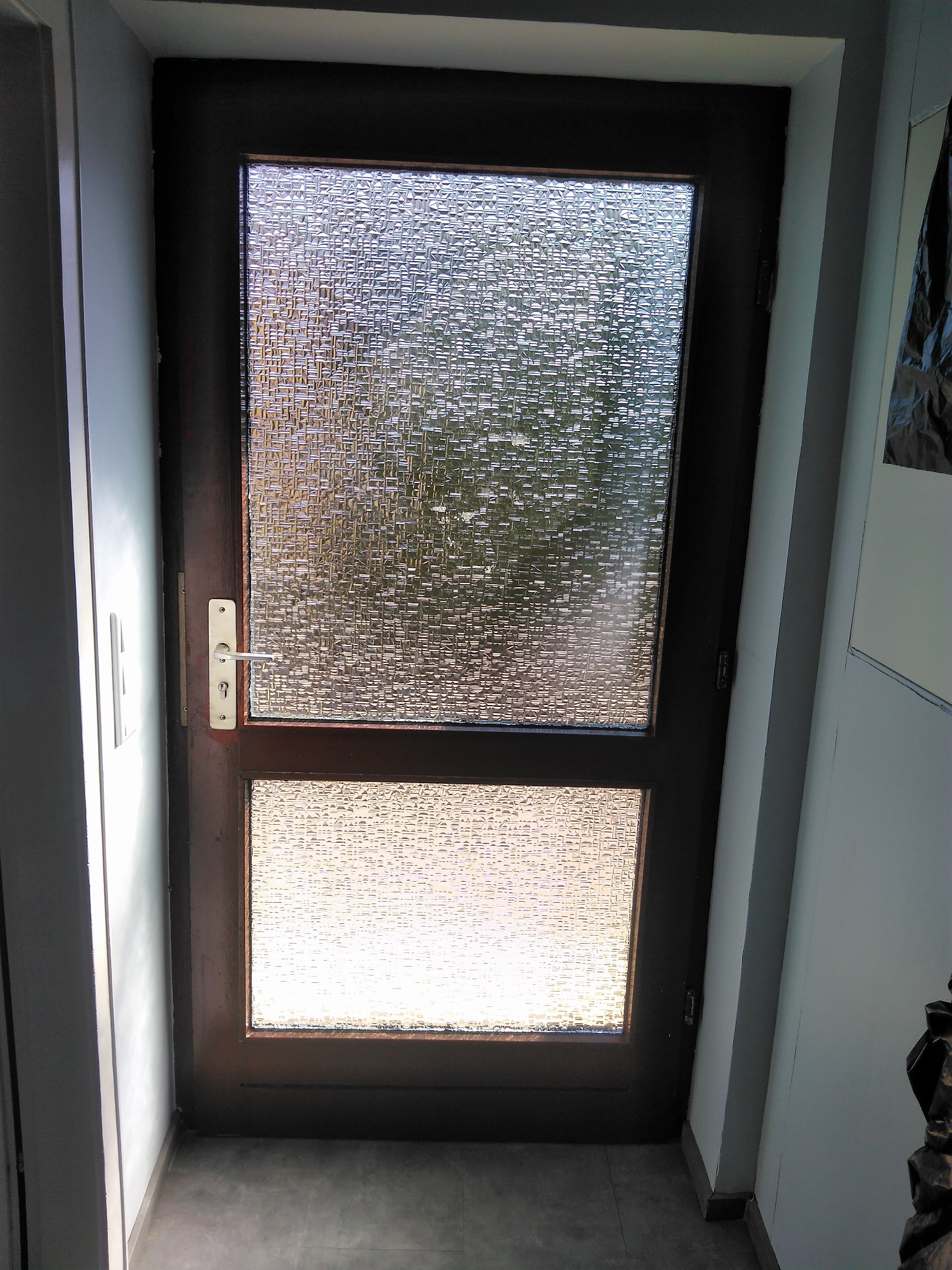 Ciemnobrązowe drzwi wewnętrzne z dwoma szybami o fakturze kostki, widoczne zamek i klamka, szara podłoga i białe ściany.