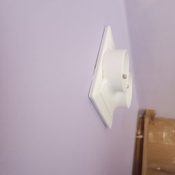 K & J Remont - Białe gniazdko elektryczne z podwójnym wejściem zamontowane na fioletowej ścianie, widoczne z boku pod kątem.