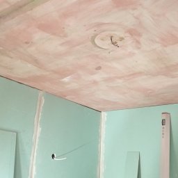 K & J Remont - Ściany z zielonej płyty gipsowo-kartonowej i sufit w trakcie szpachlowania, widoczne przewody elektryczne i drabina malarska w rogu pomieszczenia.