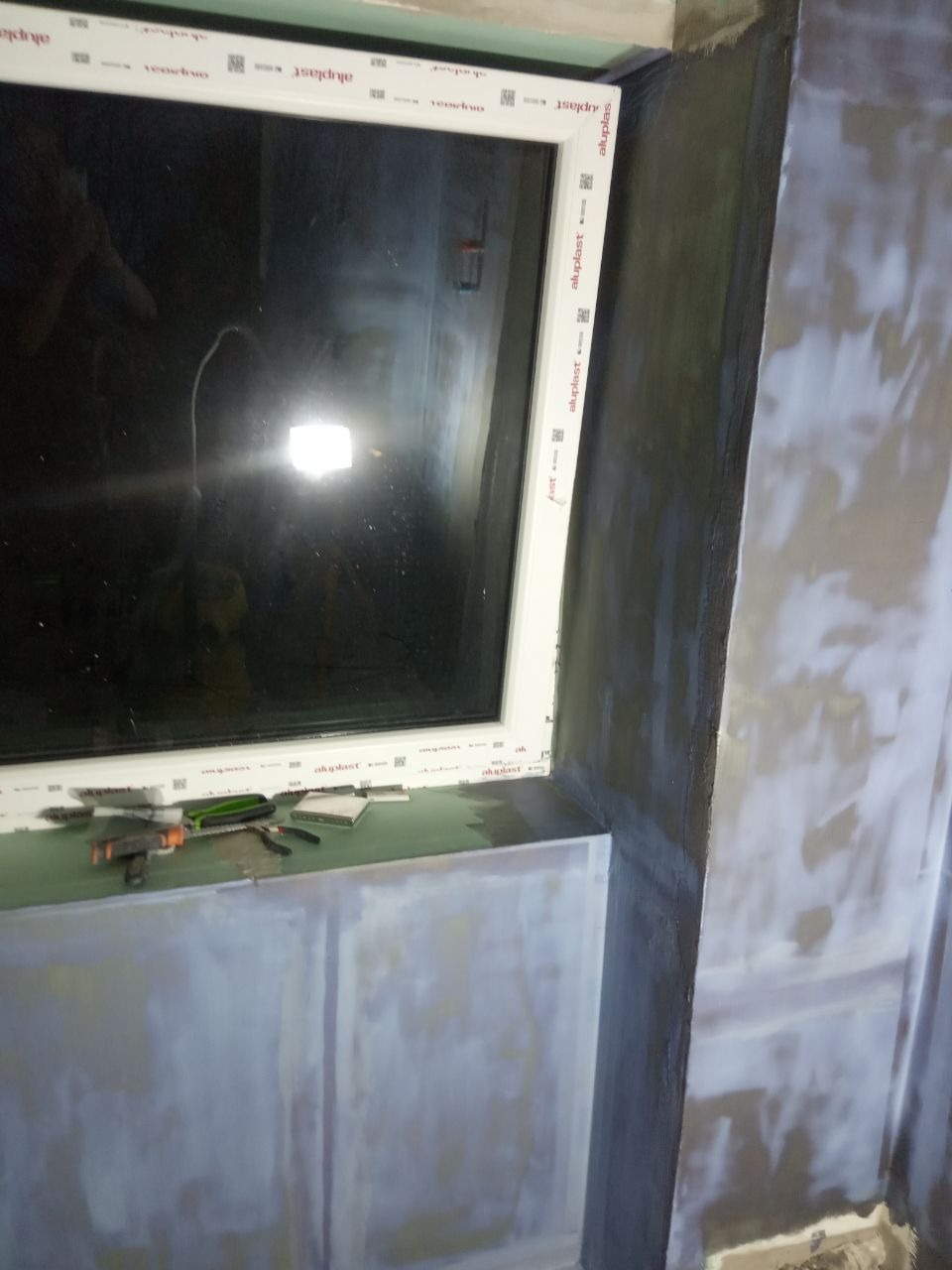 Przygotowanie ściany do malowania: szpachlowana powierzchnia wokół okna z widocznymi narzędziami na parapecie.