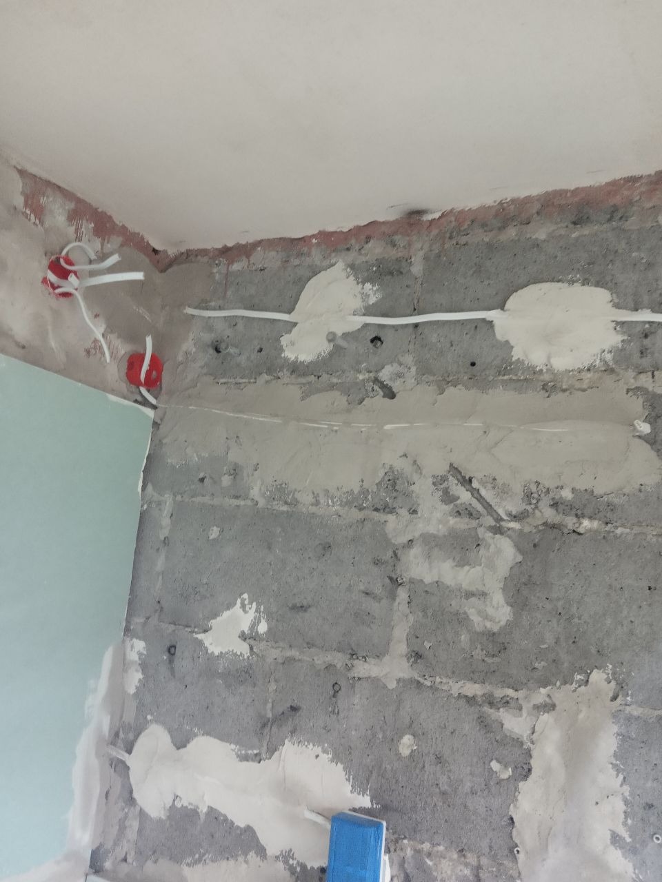 Ściana z surowych betonowych bloków w trakcie przygotowywania do dalszych prac wykończeniowych, widoczne wyprowadzone przewody elektryczne w puszkach, częściowo zaszpachlowane bruzdy po przewodach.