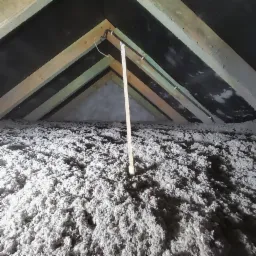 Poddasze z widoczną konstrukcją drewnianą i warstwą izolacji z wełny celulozowej, z wystającym przewodem elektrycznym zabezpieczonym peszlem.