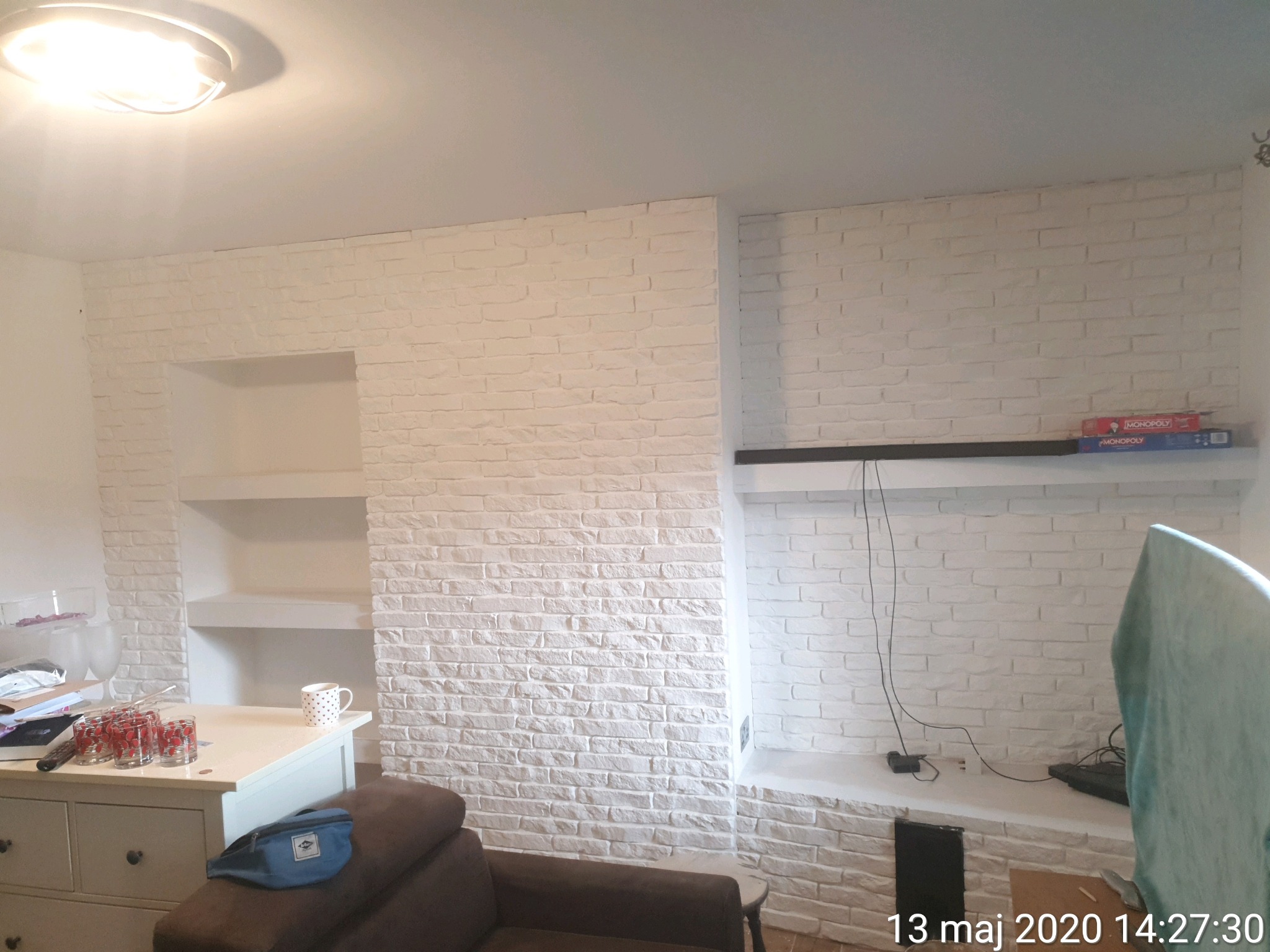 Biała ściana z cegły z wnękami w salonie w Andrychowie, na półkach książki i dekoracje.