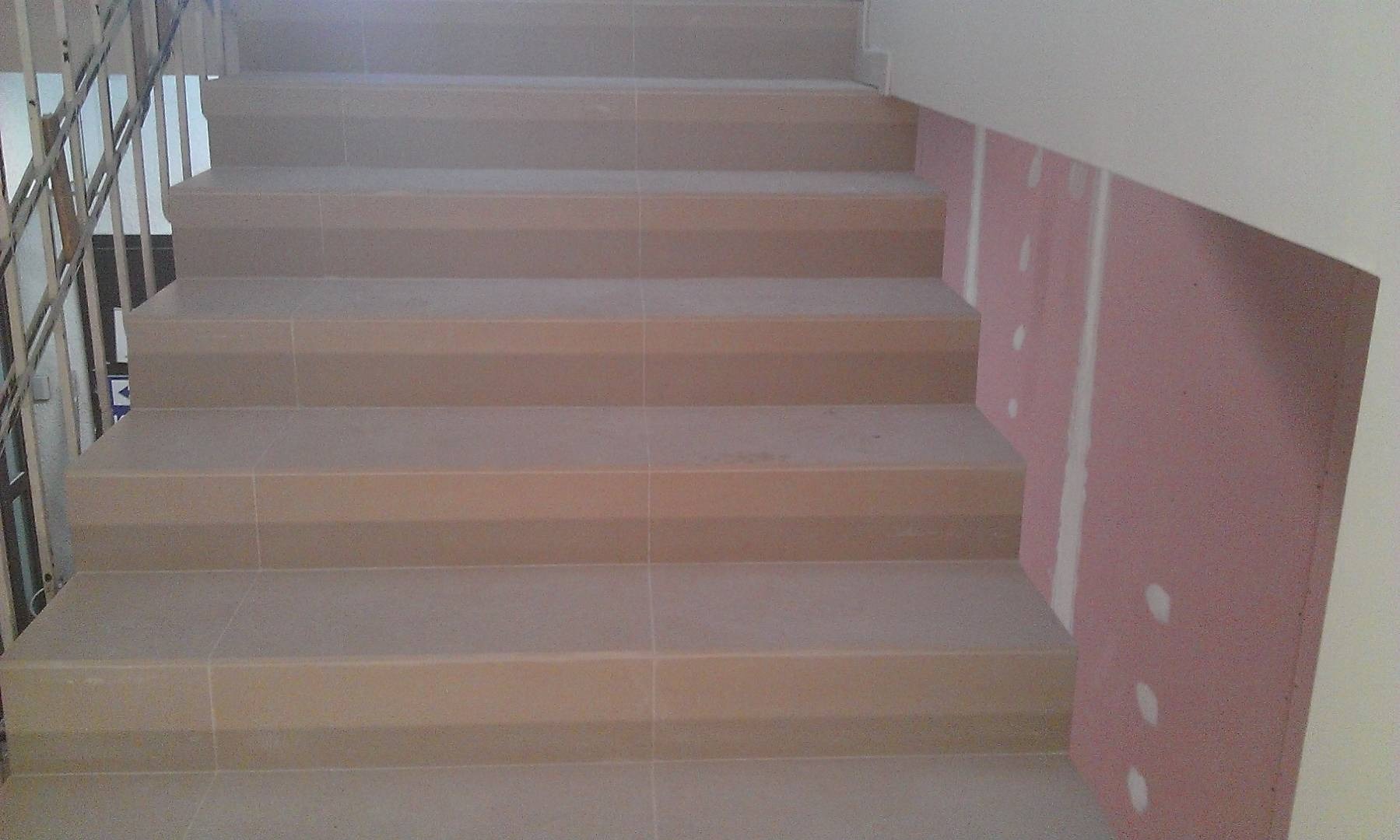 Wyłożone płytkami schody w trakcie prac wykończeniowych; widoczna płyta gipsowo-kartonowa na ścianie bocznej.