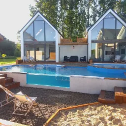 Nowoczesny dom z dużymi przeszkleniami i basenem z przezroczystą ścianą oraz piaskownicą na posesji.