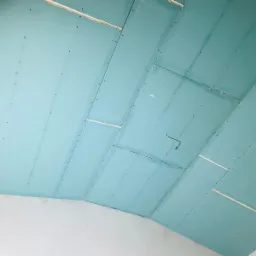 Niebieskie płyty kartonowo-gipsowe zamontowane na suficie pod skosem, widoczne wkręty, szczeliny między płytami i wystający kabel elektryczny.