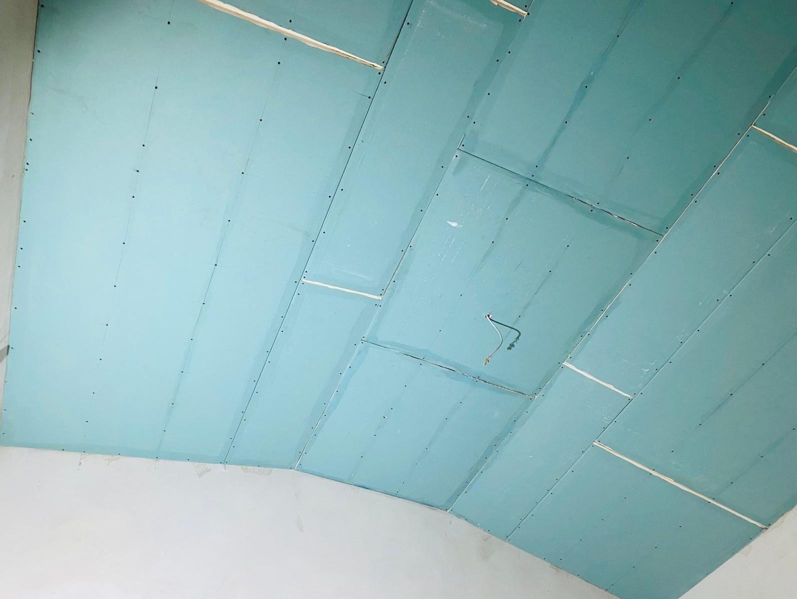 Niebieskie płyty kartonowo-gipsowe zamontowane na suficie pod skosem, widoczne wkręty, szczeliny między płytami i wystający kabel elektryczny.