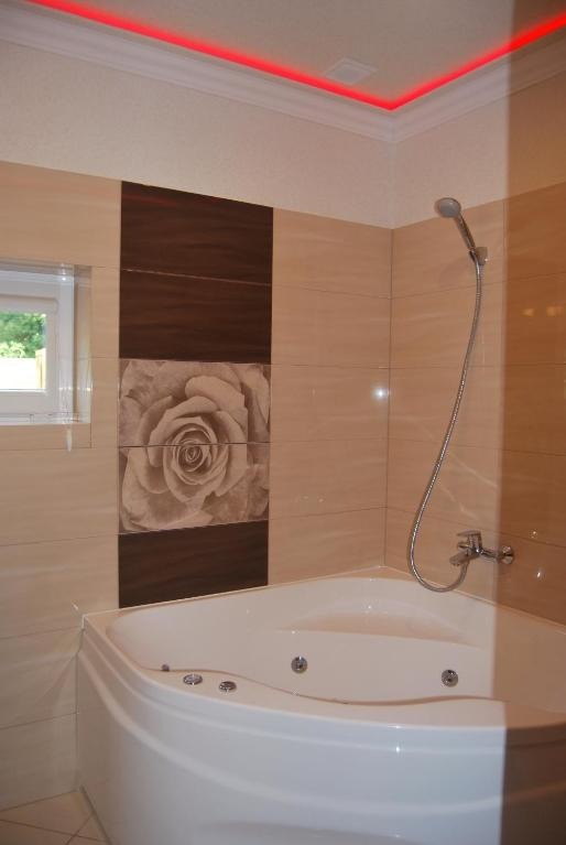Nowoczesna łazienka z narożną wanną z hydromasażem, beżowe płytki z motywem kwiatowym, oświetlenie LED w kolorze czerwonym przy suficie.