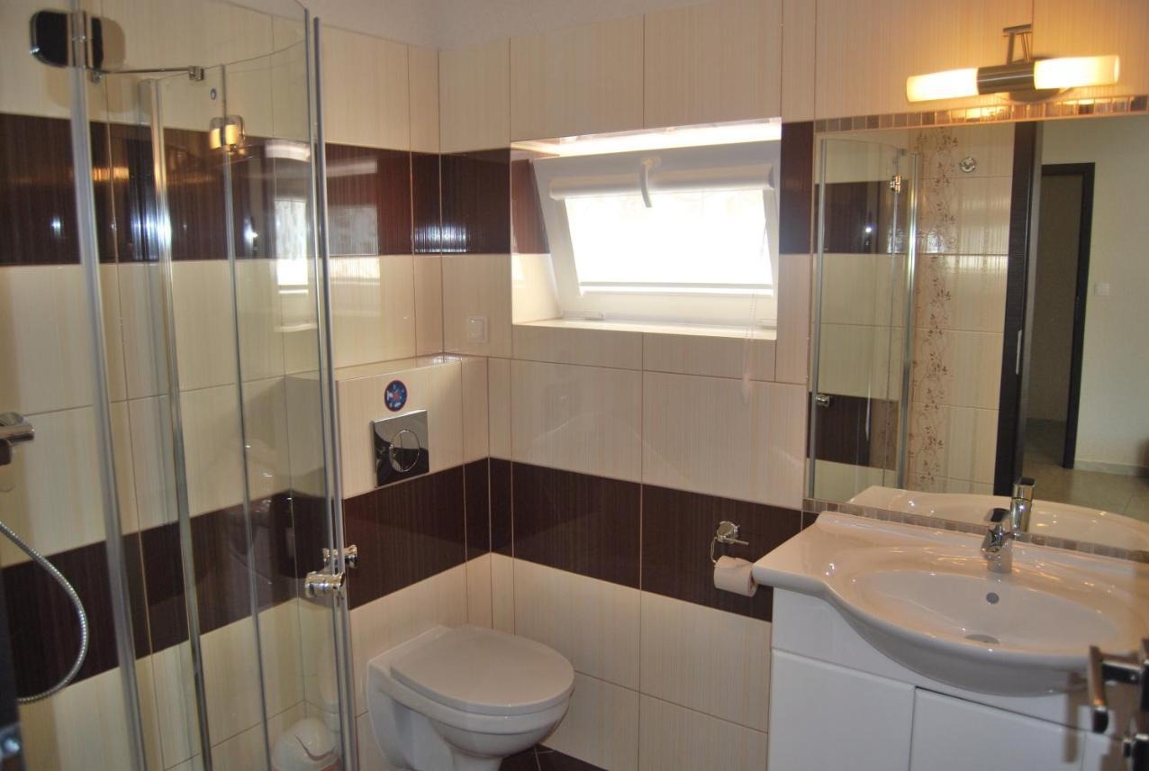 Wykończona łazienka z kabiną prysznicową, umywalką z szafką i toaletą, wykończona płytkami w odcieniach beżu i brązu z poziomymi pasami, okno dachowe z roletą.