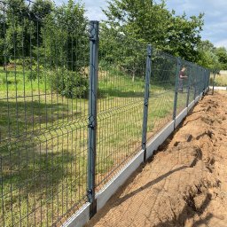 Vasylenko Viacheslav - Nowo zainstalowane, panelowe ogrodzenie z podmurówką betonową na tle zielonego ogrodu, widoczne ślady prac ziemnych.