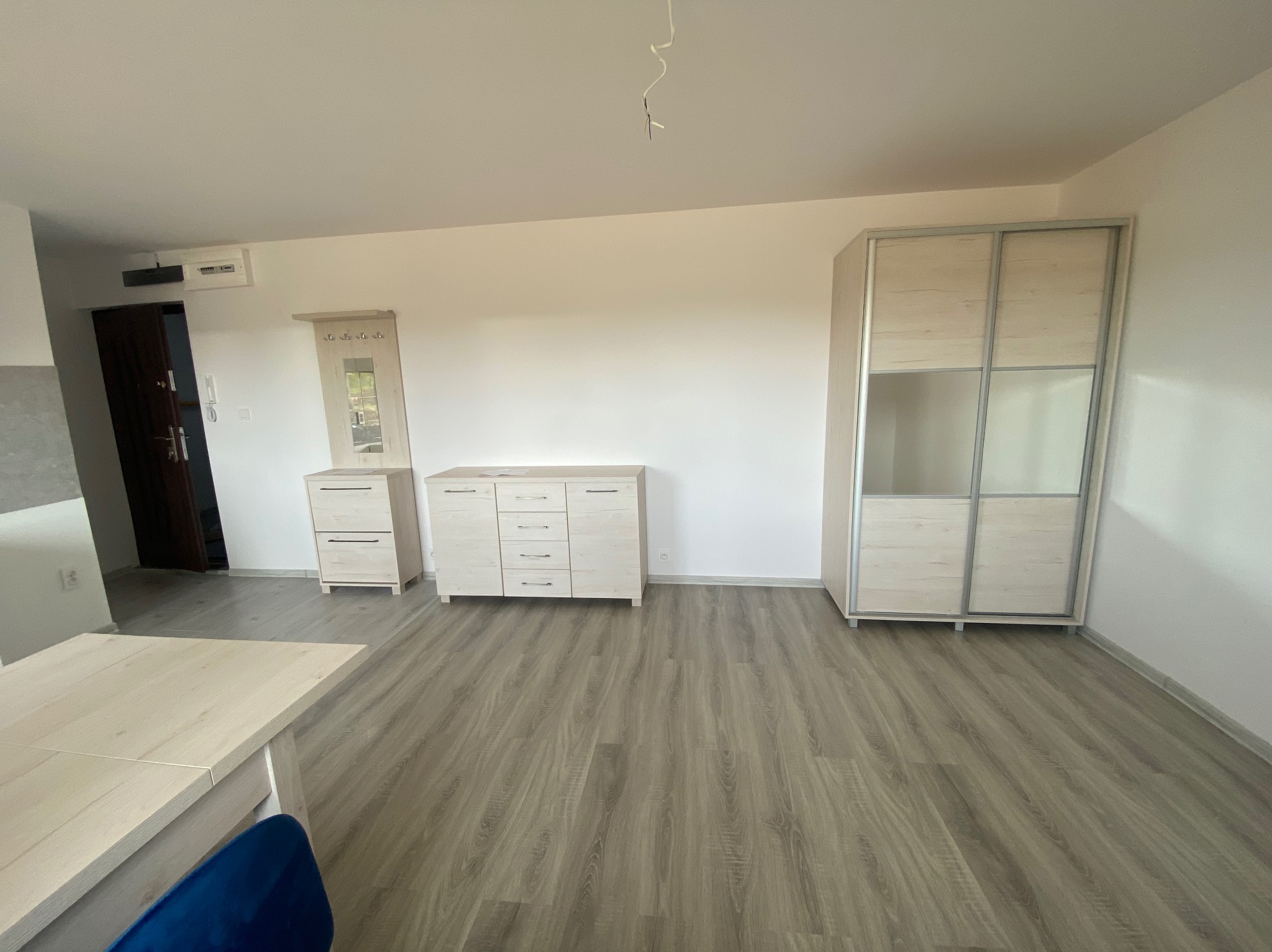 Jasne, minimalistyczne wnętrze: szafa przesuwna z lustrami, komoda z szufladami, wieszak z lustrem, stół z krzesłem na panelach podłogowych.