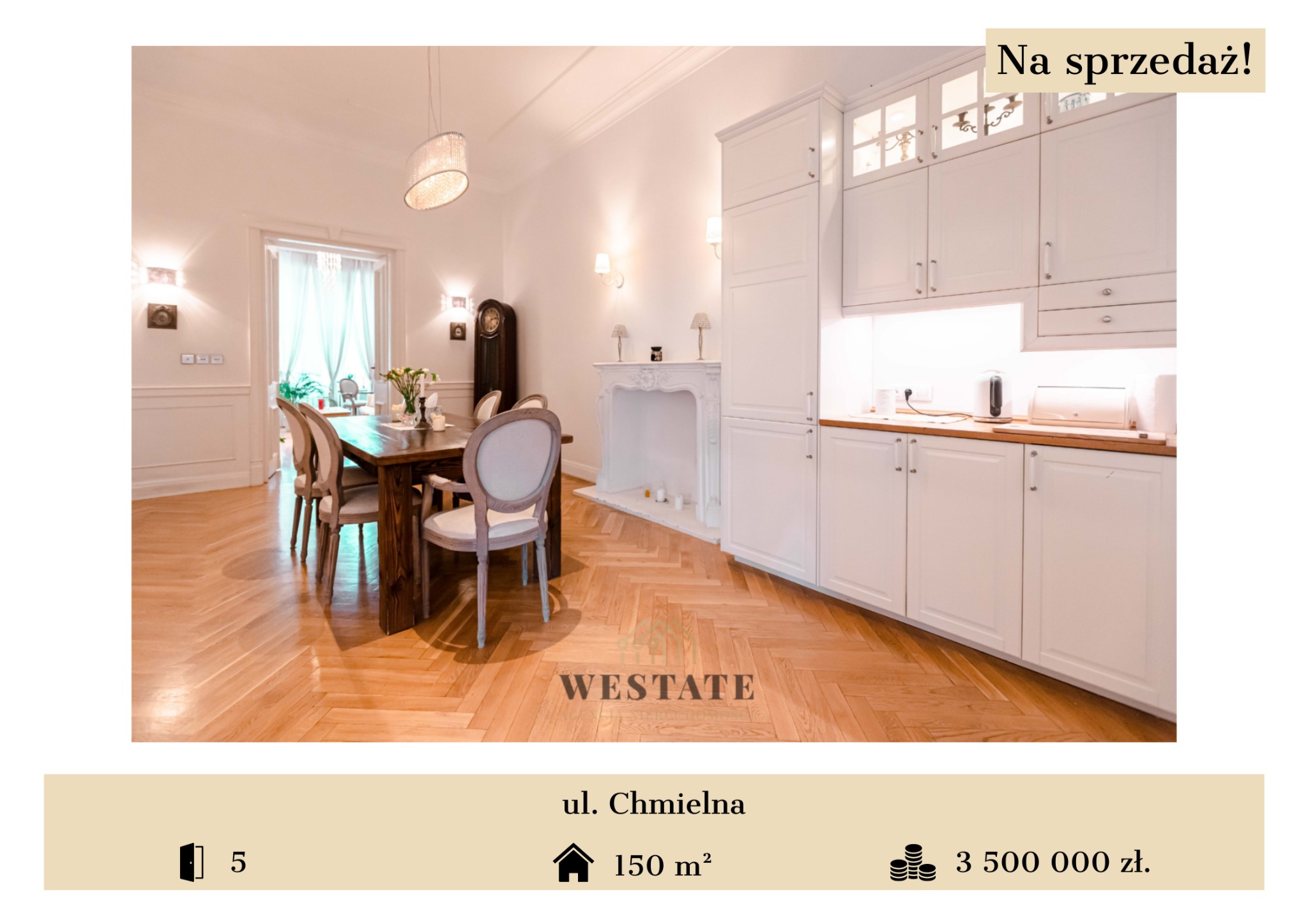 Jasne, przestronne wnętrze z drewnianą podłogą w jodełkę, dużym stołem z kwiatami, białymi krzesłami, kominkiem i zabudową kuchenną. Widoczny zegar stojący.