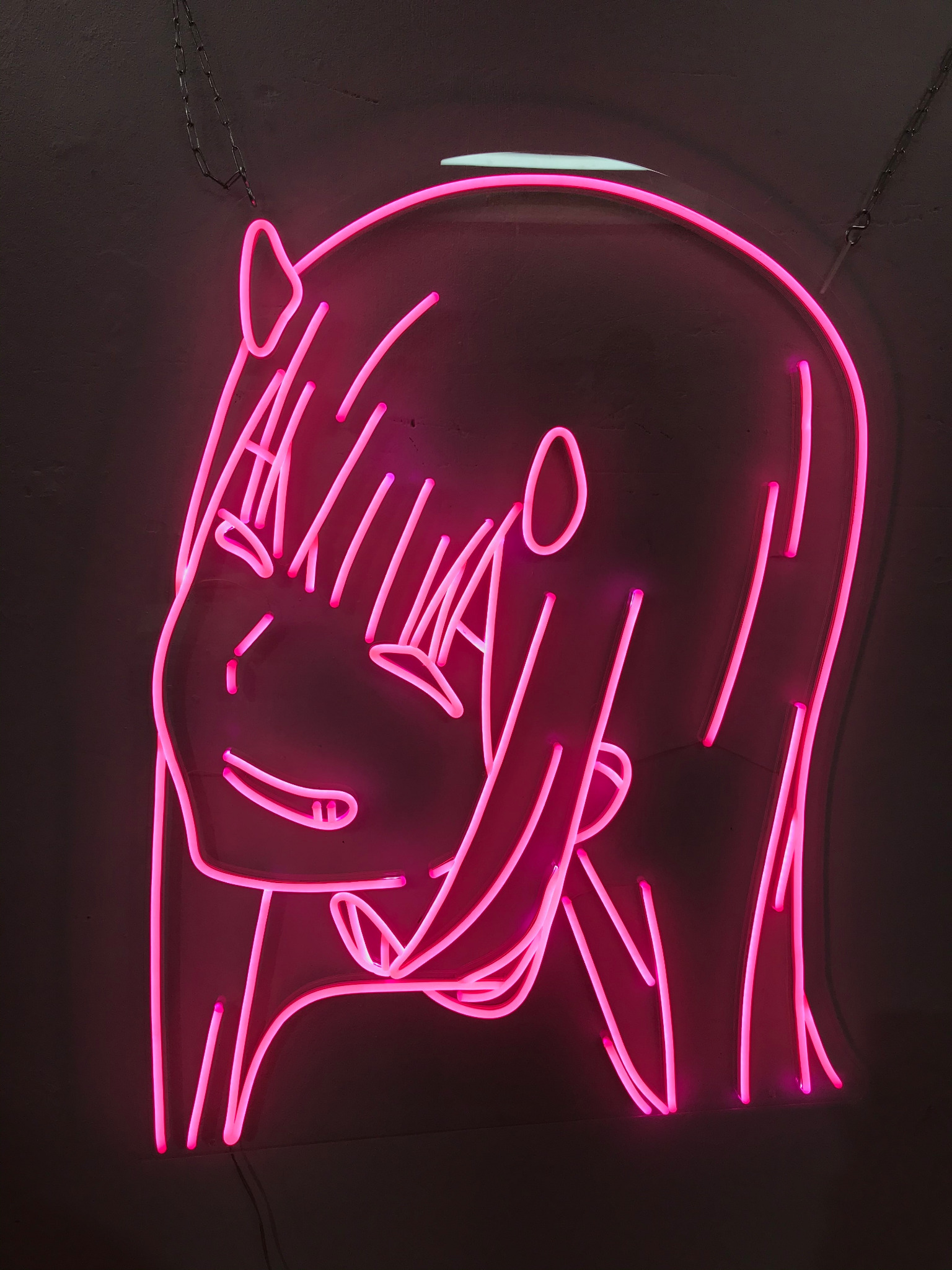 Różowy neonowy portret dziewczyny z rogami w stylu anime, zawieszony na łańcuszku na ścianie, wykonany w Warszawie.