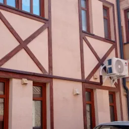 Zewnętrzna jednostka klimatyzacji marki Gree zamontowana na elewacji budynku z drewnianą konstrukcją szkieletową w stylu rustykalnym.