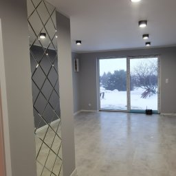 KAL-BUD Kamil Kalbarczyk - Szare wnętrze po odświeżeniu, z pionowym lustrem w romby na ścianie, szarą podłogą z płytek i oknem balkonowym z widokiem na zaśnieżony ogród.