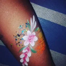 Ręka z namalowanymi farbami kwiatami i brokatem na tle niebiesko-białego ręcznika.