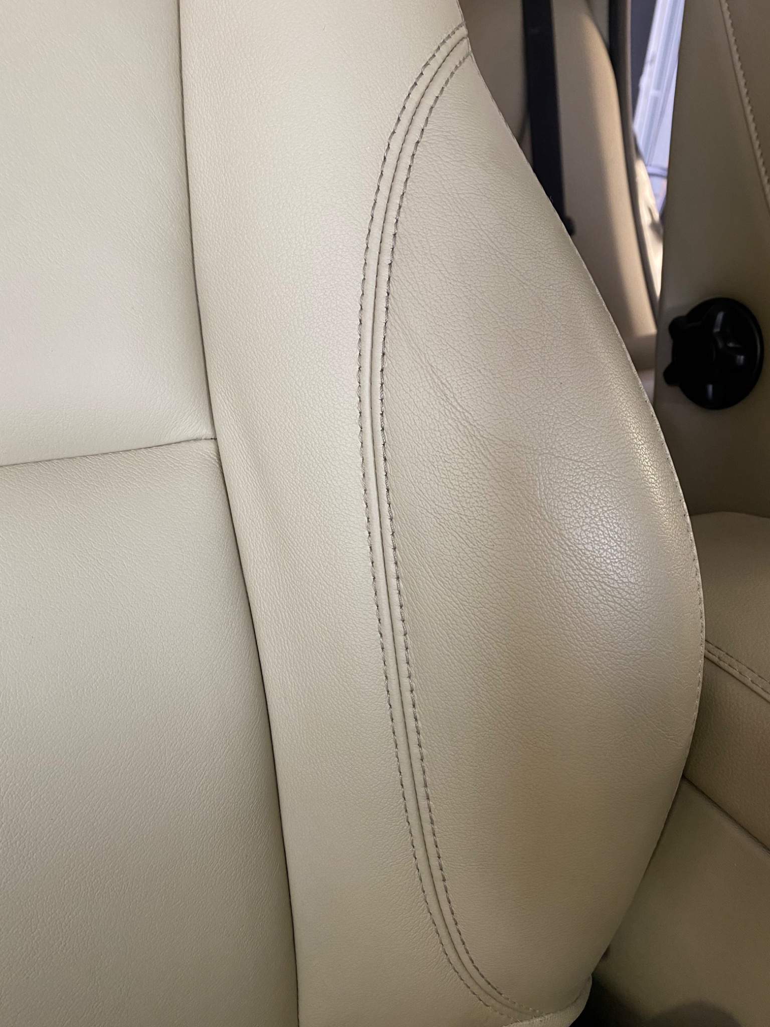 Fragment kremowego skórzanego fotela samochodowego z wyraźnym szwem, widoczny wnętrze pojazdu w tle, Poznań.