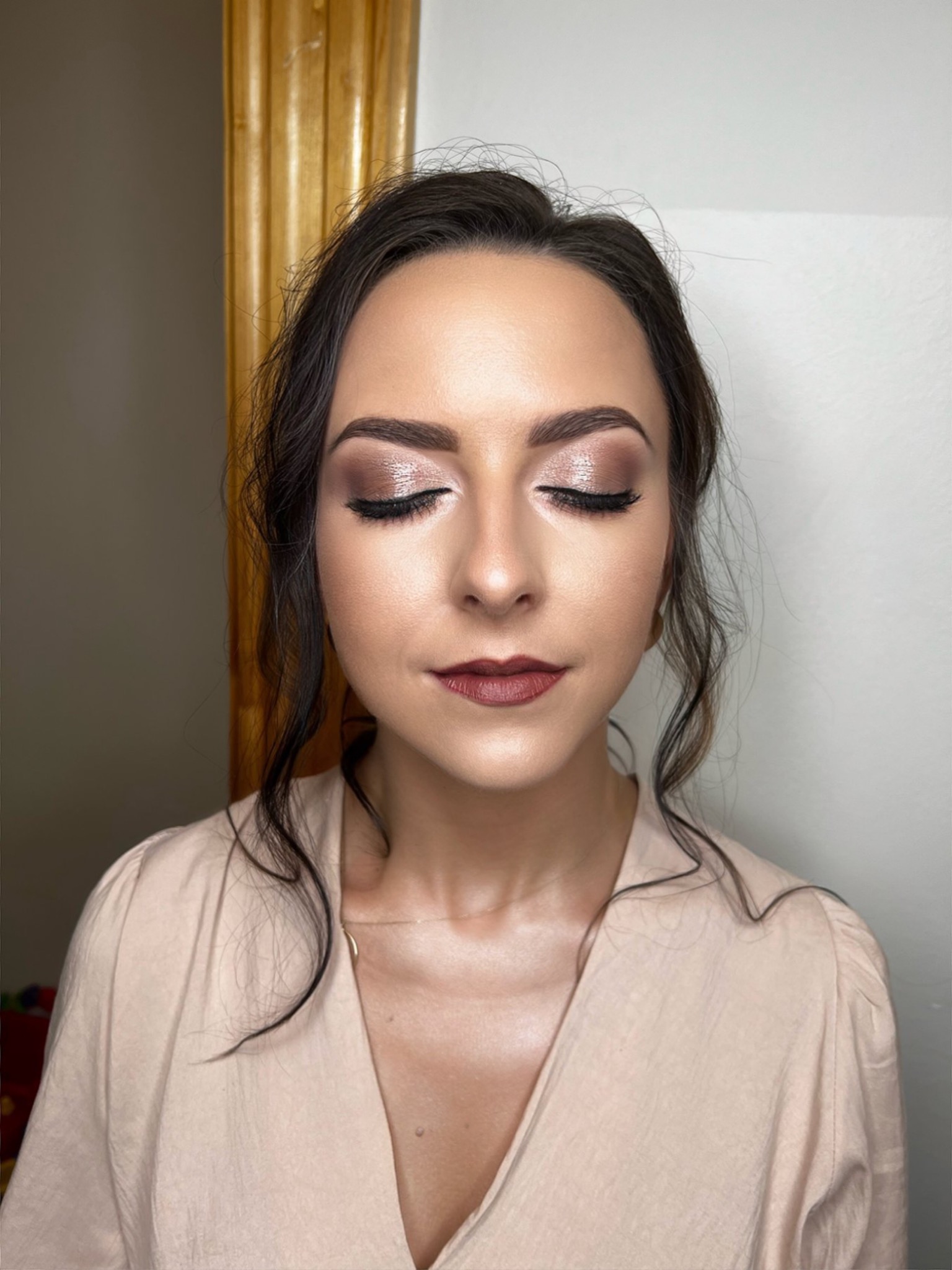 Portret kobiety z zamkniętymi oczami, prezentującej delikatny, błyszczący makijaż oczu w odcieniach brązu i różu, z wyraźnie podkreślonymi rzęsami i ustami w kolorze ciemnej czerwieni. Tło jest...