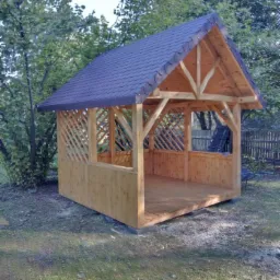 Nowa, drewniana altana z ciemnym, łuskowym dachem, otoczona zielenią ogrodu, widziana w słoneczny dzień.