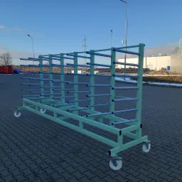 Wielopoziomowy, metalowy regał na kółkach w kolorze miętowym z szarymi poprzeczkami, przeznaczony do przechowywania długich elementów, ustawiony na brukowanym placu.