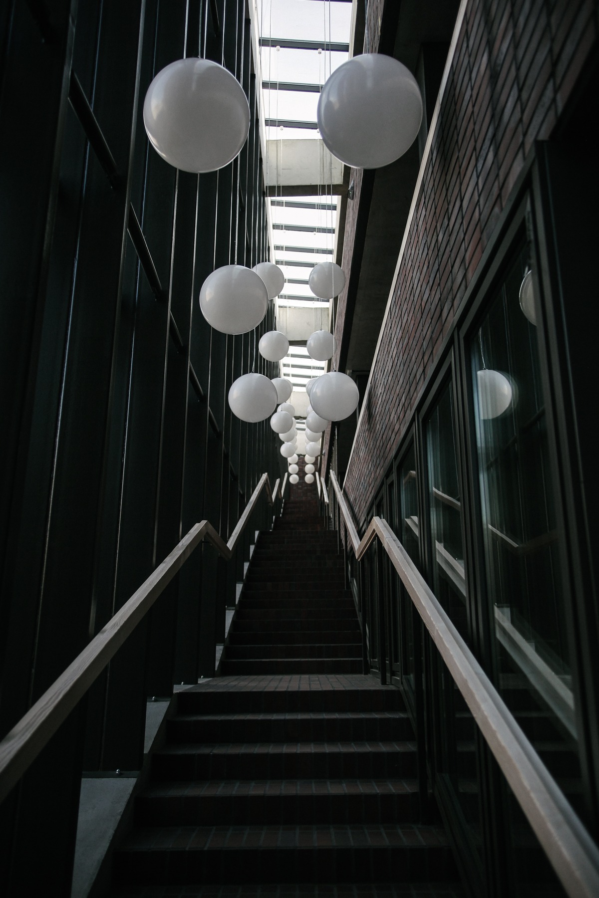 Wysokie schody z cegły w budynku usługowym, oświetlone przez okno dachowe i dekorowane wiszącymi kulami.