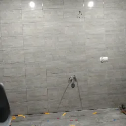 Układanie szarych płytek w łazience, widoczne krzyżyki dystansowe i wiadro z zaprawą, przygotowane do fugowania.