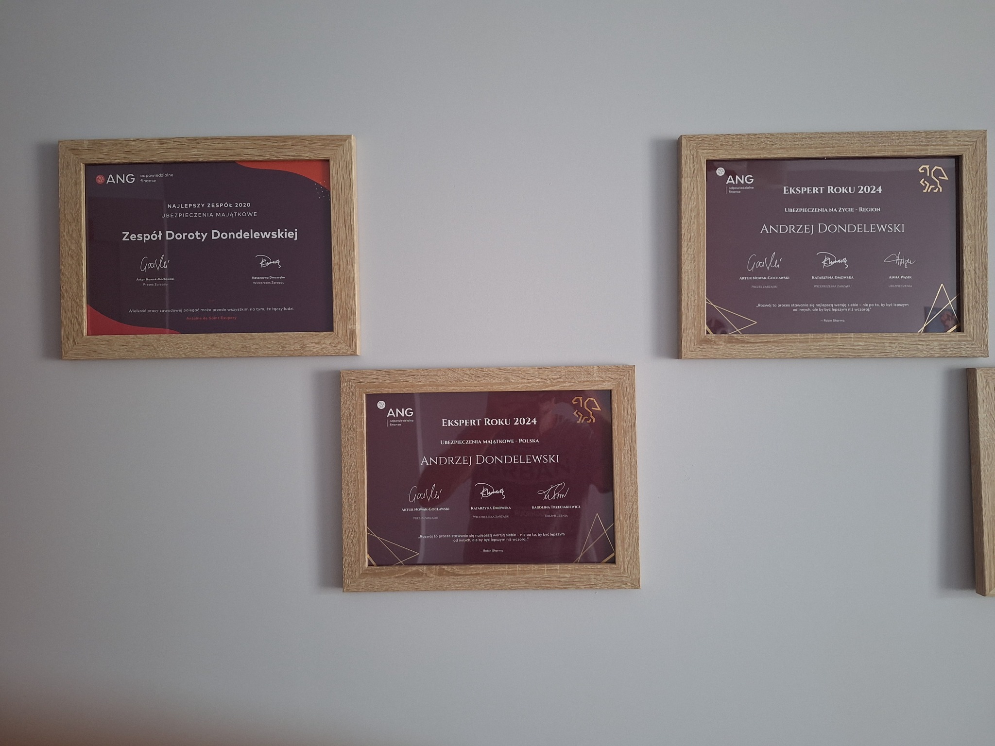 Oprawione certyfikaty firmy ANG, potwierdzające nagrody i tytuły eksperta dla zespołu i osoby, wiszące na ścianie. Nagrody z zakresu ubezpieczeń majątkowych i na życie.