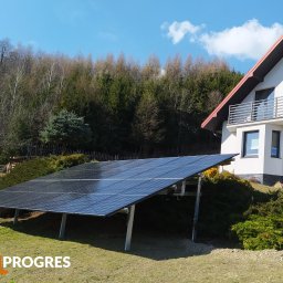 SolProgres - Panel słoneczny na gruncie przed domem jednorodzinnym z widocznym logo firmy instalacyjnej w rogu kadru.