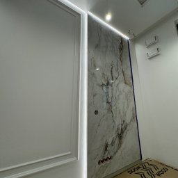 ElektroBud - Ściana z marmurowym panelem podświetlonym listwą LED, obok ściana z dekoracyjną sztukaterią, widoczne przygotowane otwory na gniazdka elektryczne i wystające przewody.