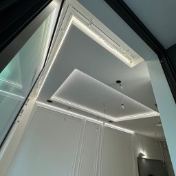 ElektroBud - Nowoczesne wnętrze z podwieszanym sufitem z oświetleniem LED, widoczne przygotowania do montażu lamp wiszących, ściany z dekoracyjnymi panelami.