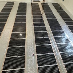 ElektroBud - Maty grzewcze pod podłogę ułożone równolegle na wylewce, widoczne kable i folia aluminiowa, przygotowanie do dalszych prac wykończeniowych.