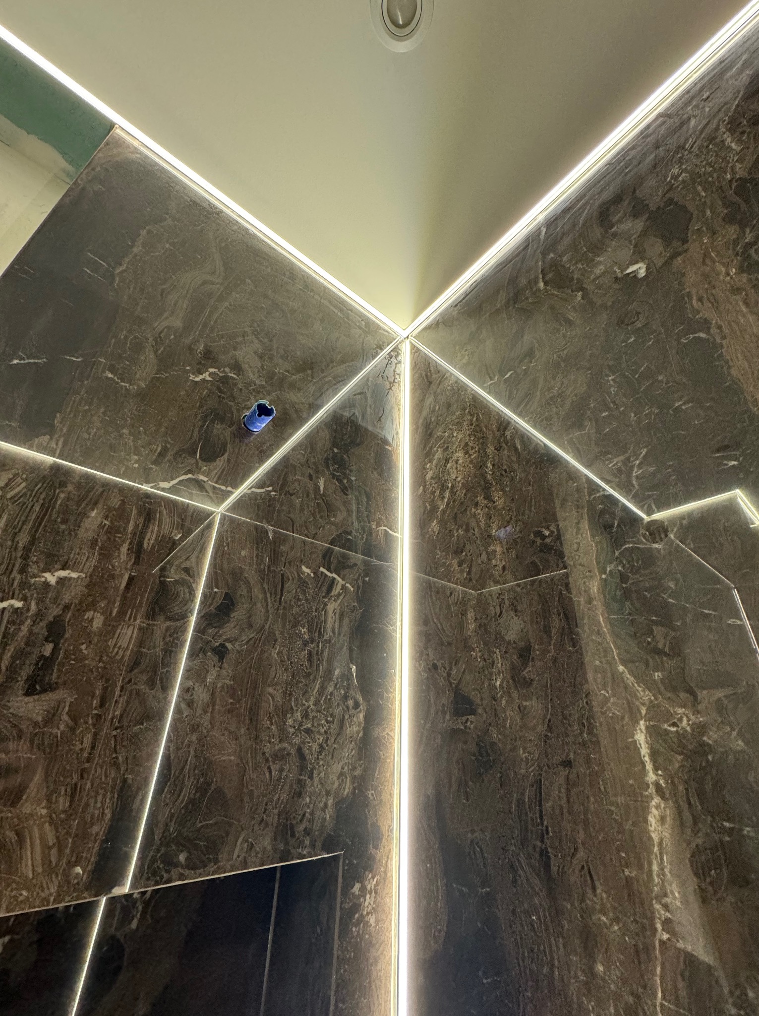 Ściany i sufit wykończone marmurem z wbudowanym oświetleniem LED tworzącym geometryczny wzór. Widoczna puszka elektryczna w ścianie.