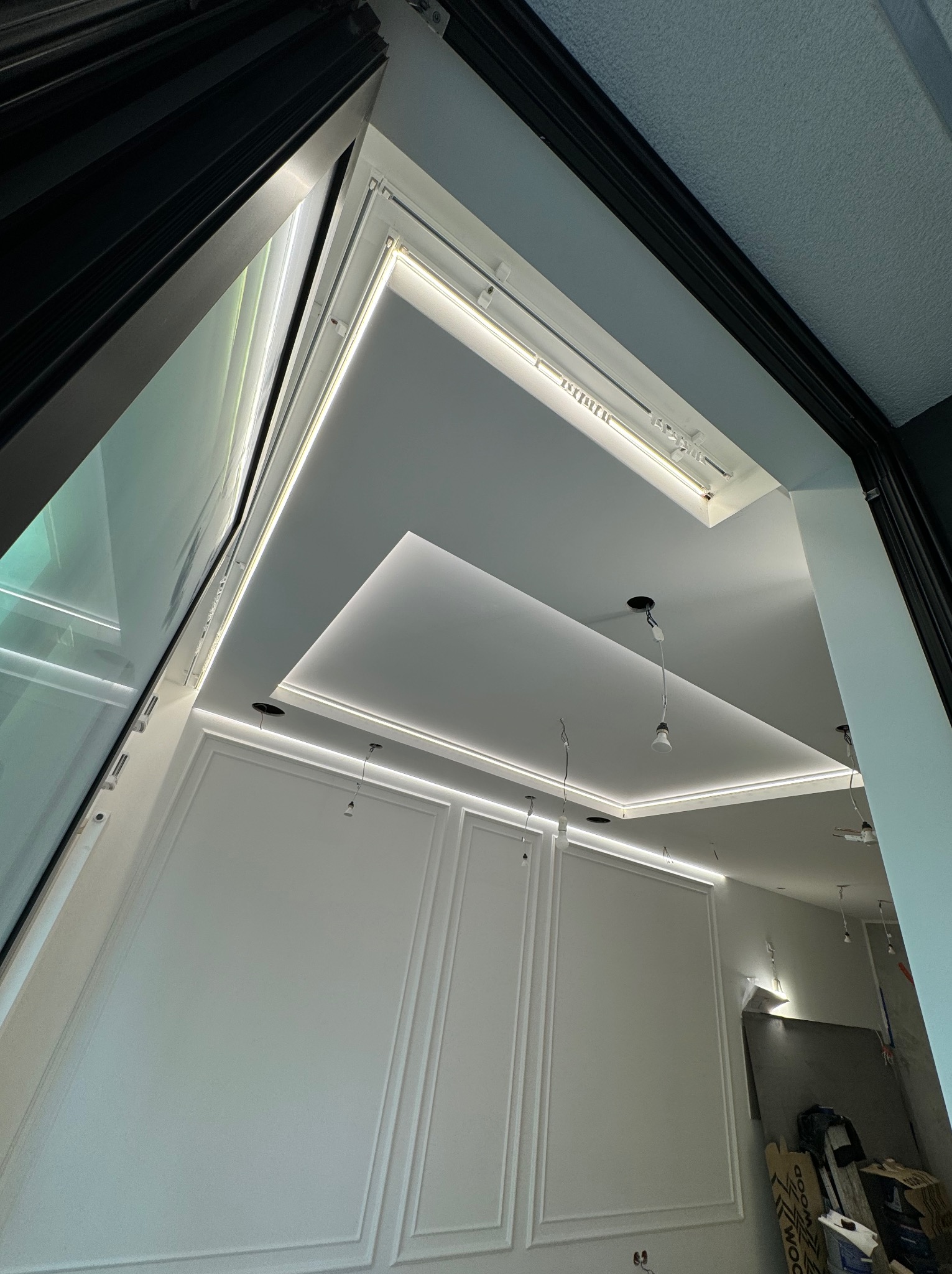 Nowoczesne wnętrze z podwieszanym sufitem z oświetleniem LED, widoczne przygotowania do montażu lamp wiszących, ściany z dekoracyjnymi panelami.