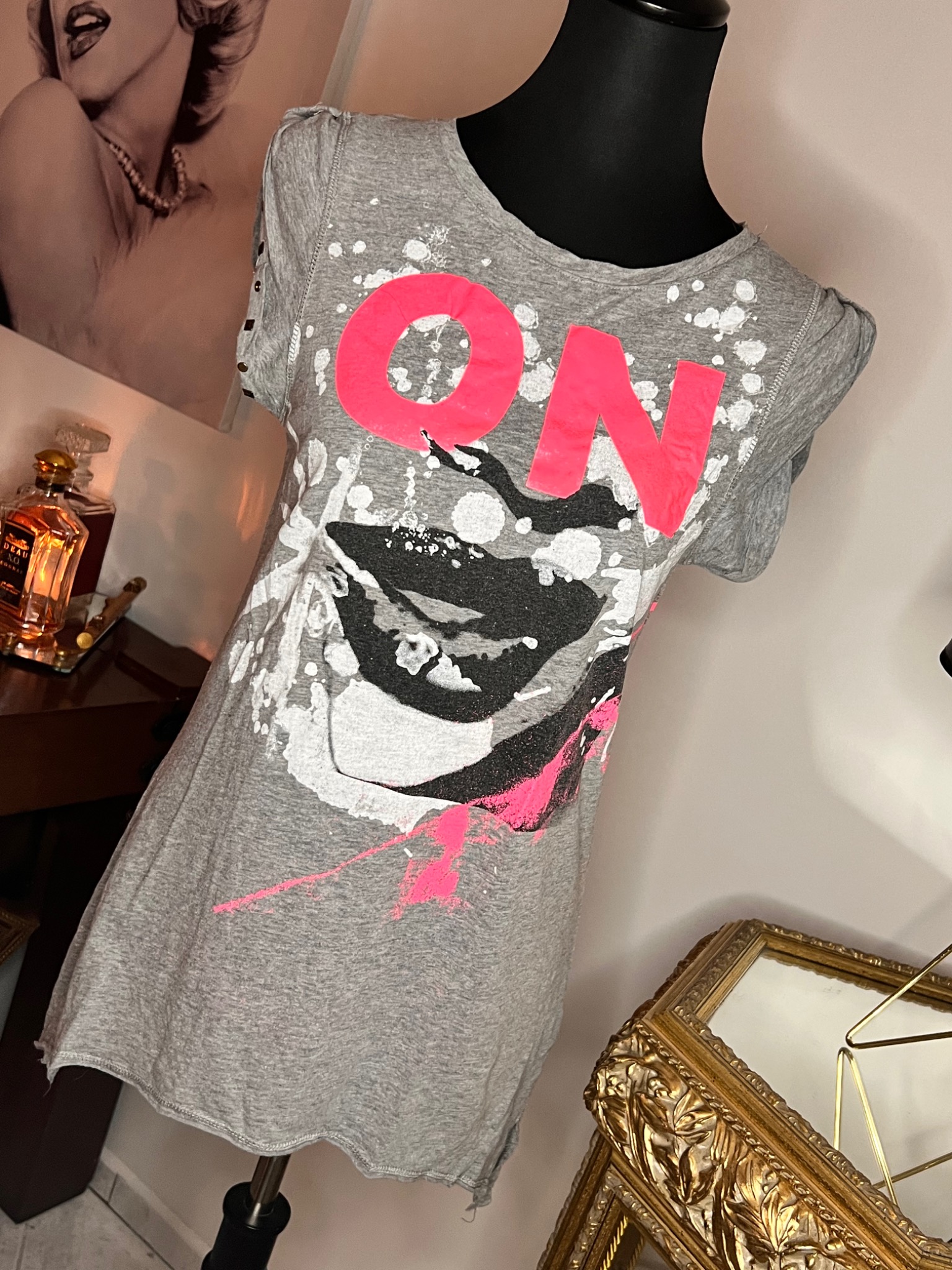 Szara, bawełniana tunika damska z różowym napisem 'ON' i abstrakcyjnym wzorem, prezentowana w Mierzynie na manekinie na tle portretu Marilyn Monroe i ozdobnego lustra.
