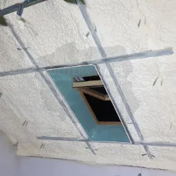 Poddasze ocieplone pianą, widoczne metalowe profile pod konstrukcję gipsowo-kartonową i okno dachowe.