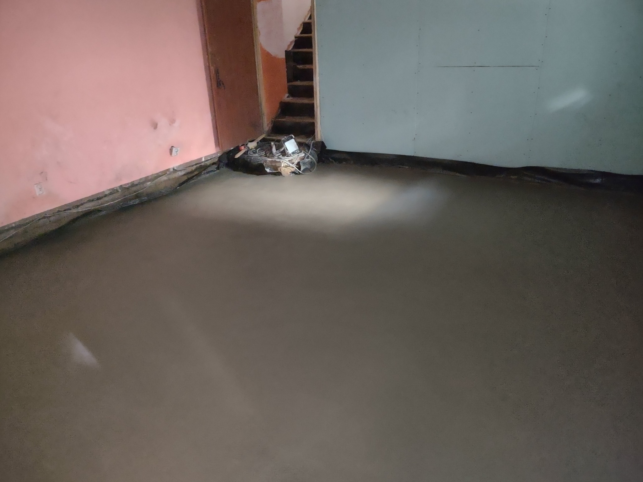 Wylewka podłogowa w trakcie schnięcia w pomieszczeniu w Słupsku, widoczne fragmenty ścian w kolorze różowym i szarym oraz schody w tle.