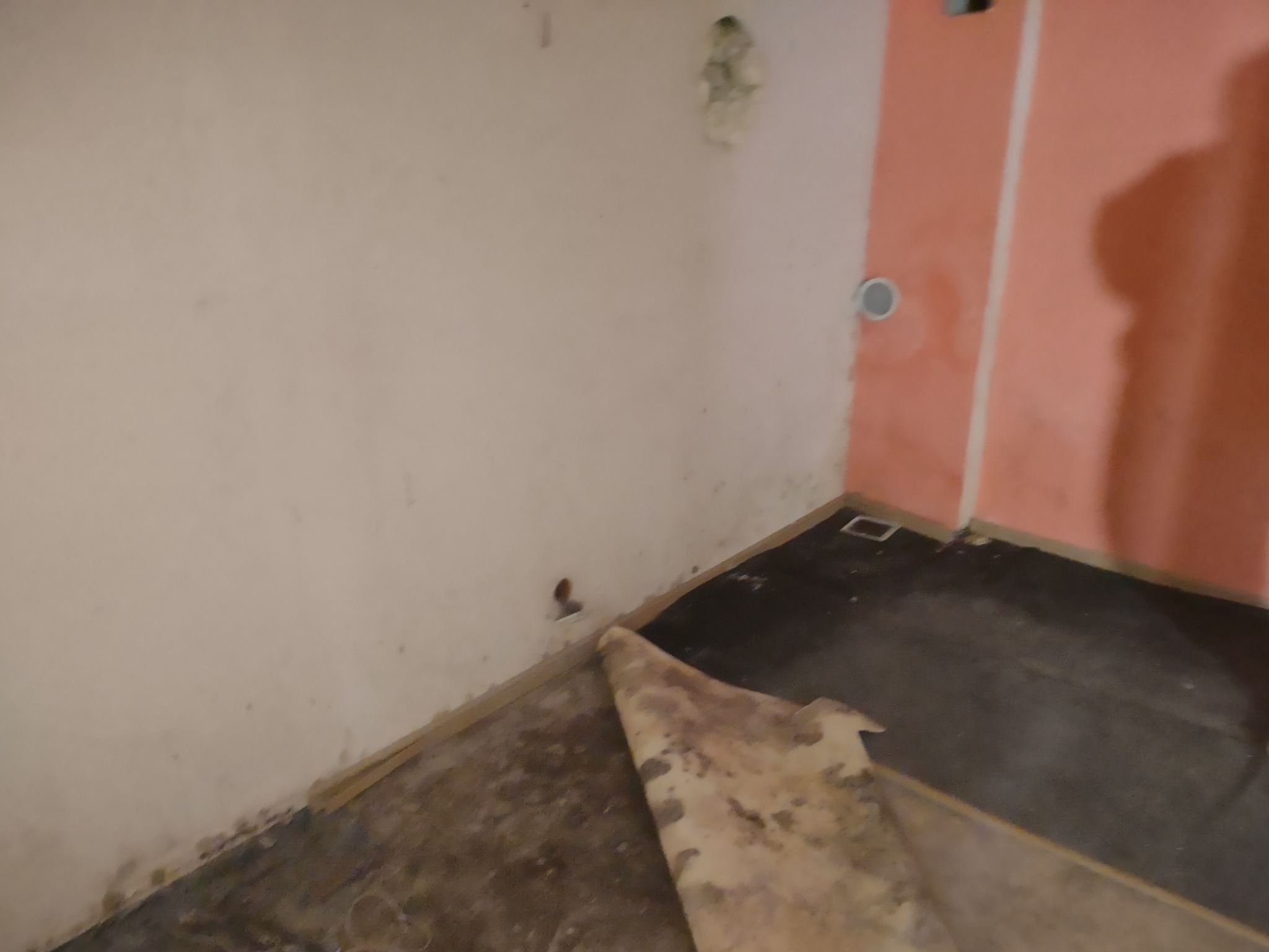 Przygotowanie podłoża pod nową podłogę w rogu pomieszczenia: usunięta stara wykładzina odsłania brudną posadzkę, ściany z widocznymi śladami po naprawach.