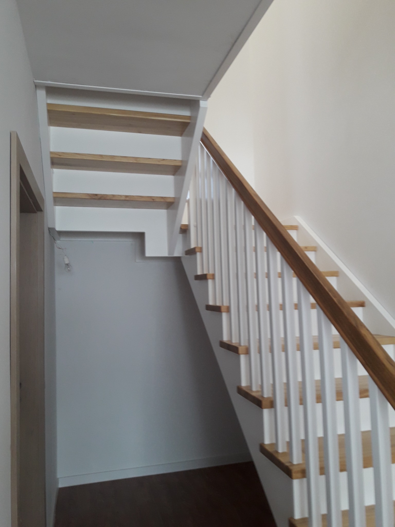 Jasne schody z drewnianymi stopniami i białą balustradą w nowoczesnym wnętrzu, widok z dołu.