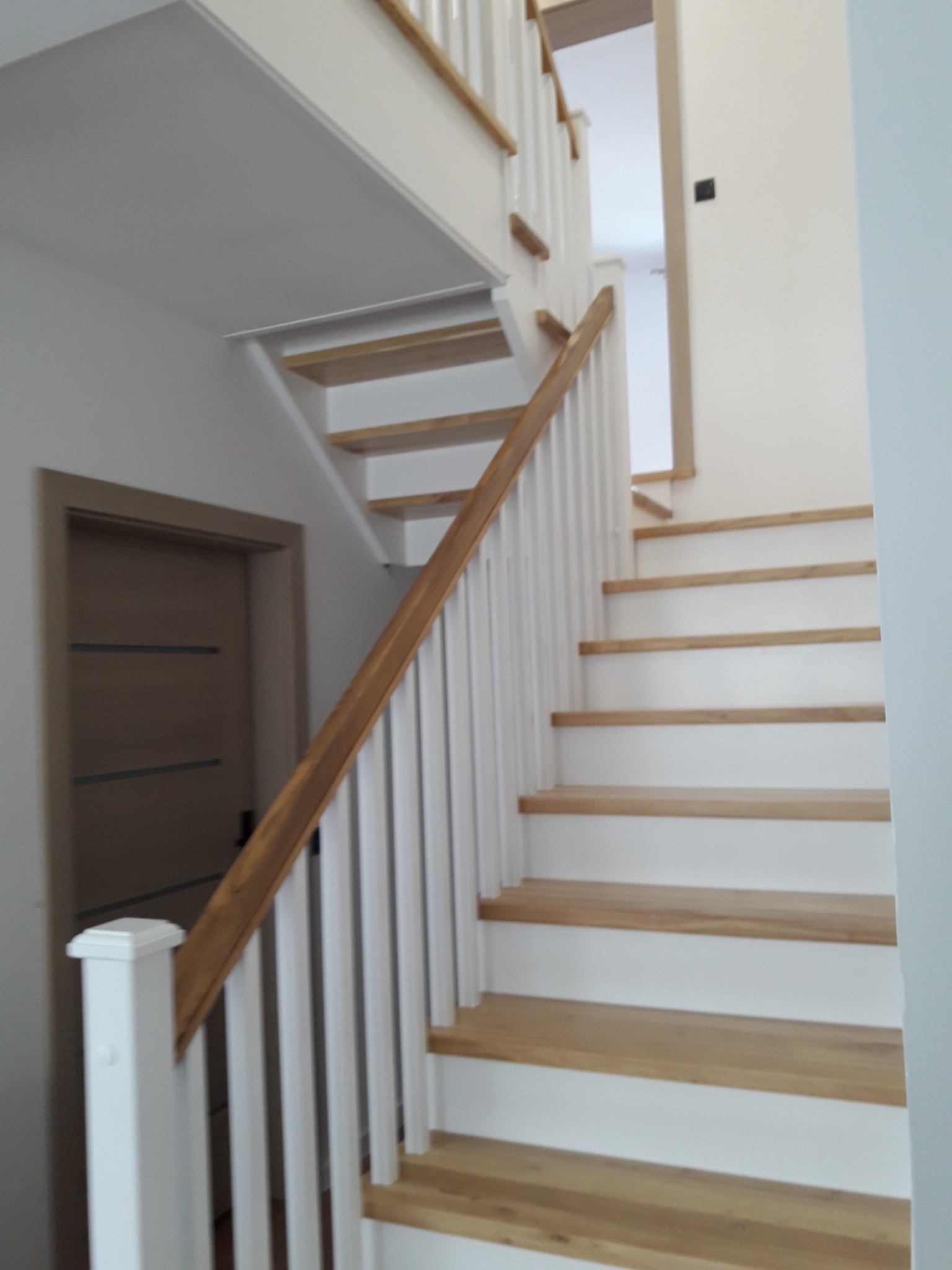 Jasne, drewniane stopnie z białymi podstopnicami i balustradą, widok z dołu na bieg schodów w jasnym wnętrzu.