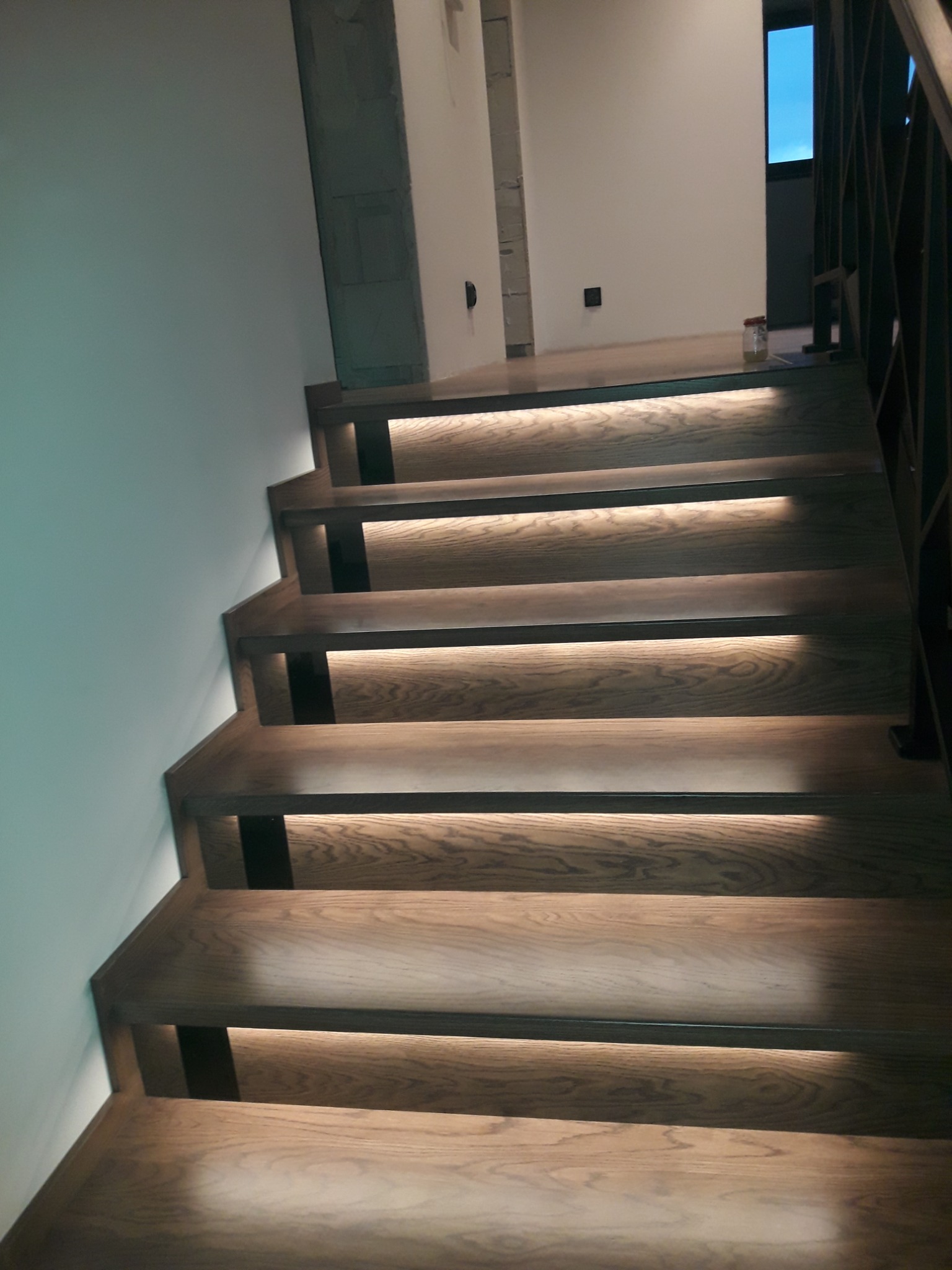 Nowoczesne, dębowe stopnie z podświetleniem LED zamontowanym pod każdym stopniem, prowadzące do góry, widoczne z dołu.