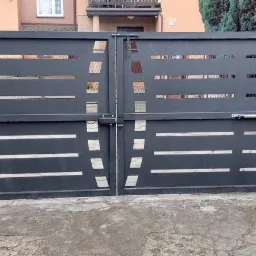 Nowoczesna, dwuskrzydłowa brama wjazdowa w kolorze grafitowym z poziomymi, ażurowymi elementami, wyposażona w siłowniki automatyki, zamontowana na zielonych słupkach.