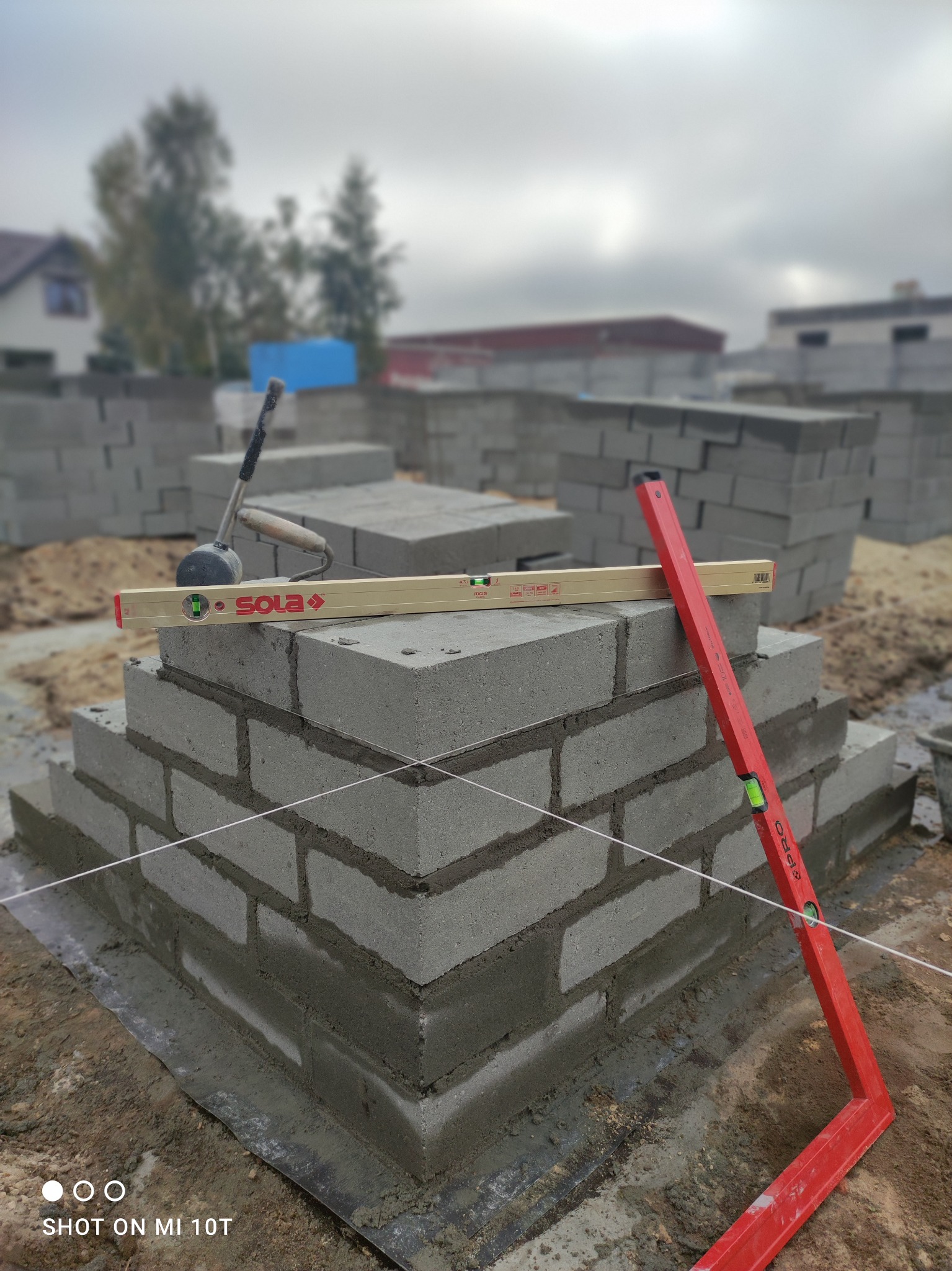 Wznoszenie muru z bloczków betonowych z użyciem poziomicy Sola i PRO, sznurek murarski naciągnięty, widoczny etap budowy ścian fundamentowych.